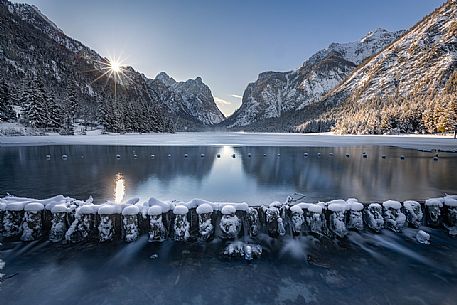 The sun rises from behind the mountains of Dobbiaco lake, Pusteria valley, dolomites, Trentino Alto Adige, Italy, Europe
