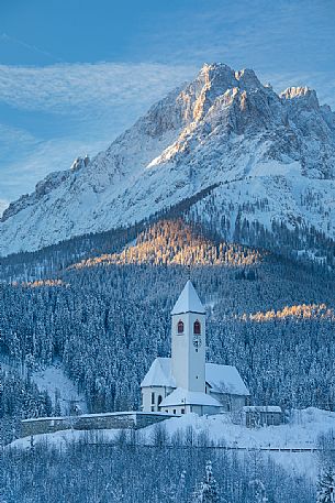 The church of the village of Versciaco after an intense snowfall, in the background the Rocca dei Baranci peak illuminated at dawn, Innichen, dolomites, Pusteria valley, Trentino Alto Adige, Italy, Europe