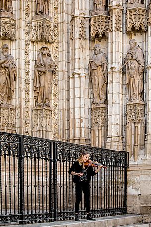 A street artist plays the violin under the facade of the Cathedral of Seville or Church of Santa Maria della Sede, Seville, Spain, Europe