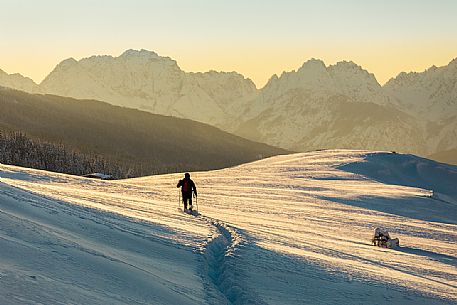 Hiker with the snowshoes at the first light of dawn, on background the Comelico mountains, Pusteria valley, dolomites, Trentino Alto Adige, Italy, Europe