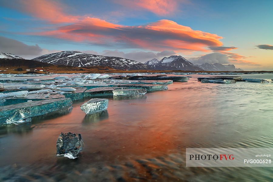 Pieces of ice, stranded on the beach reflect the colors and the light of dawn