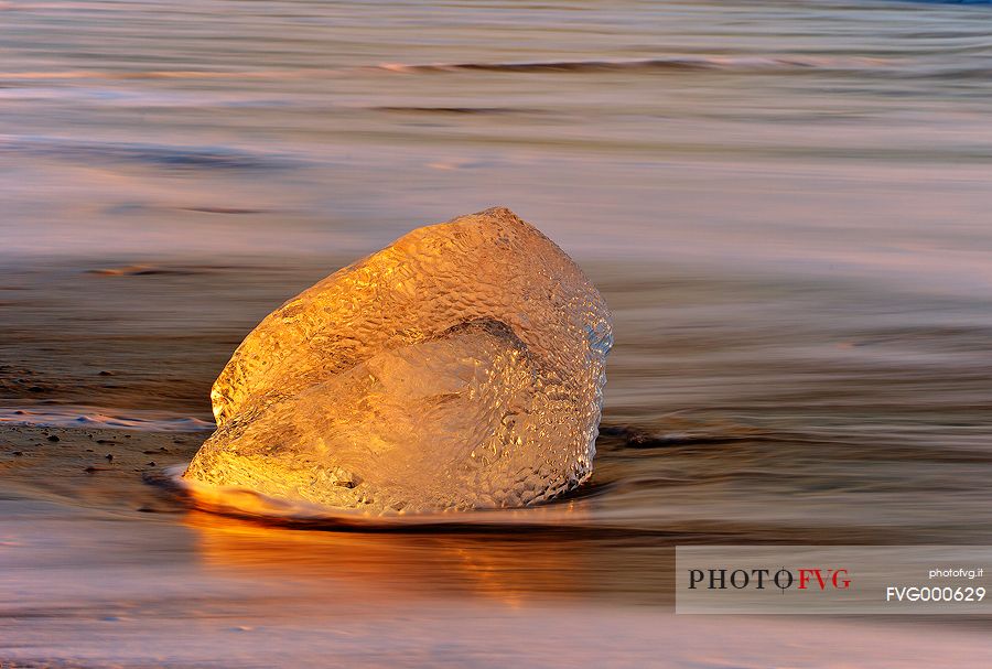 Pieces of ice, stranded on the beach reflect the colors and the light of dawn