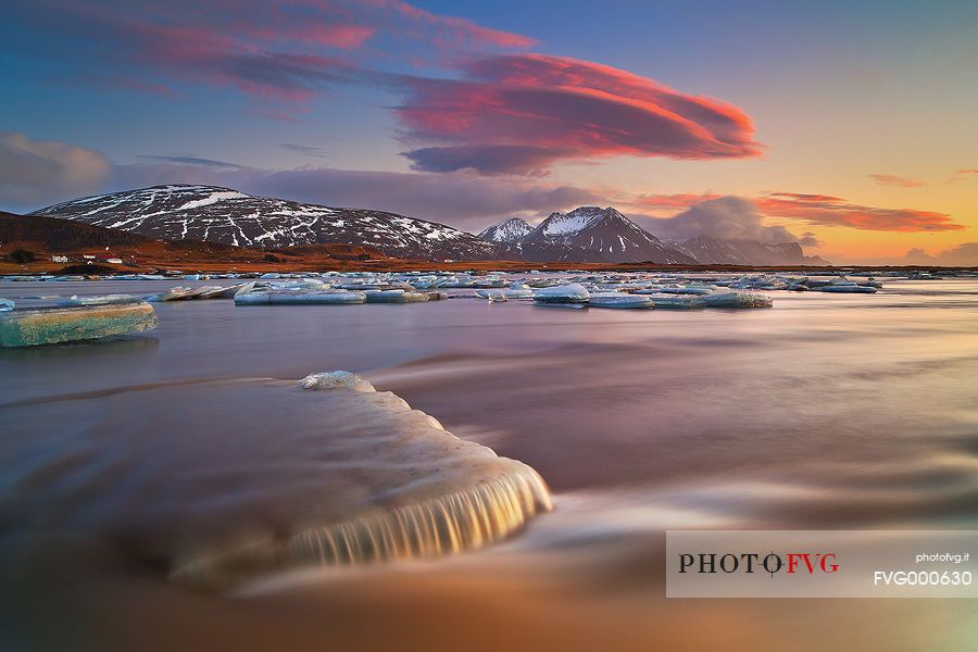 Pieces of ice, stranded on the beach reflect the colors and the light of dawn