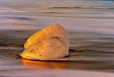 Pieces of ice, stranded on the beach reflect the colors and the light of dawn