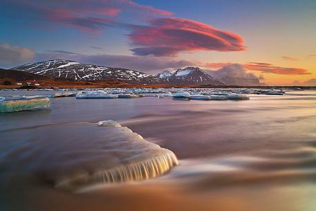 Pieces of ice, stranded on the beach reflect the colors and the light of dawn