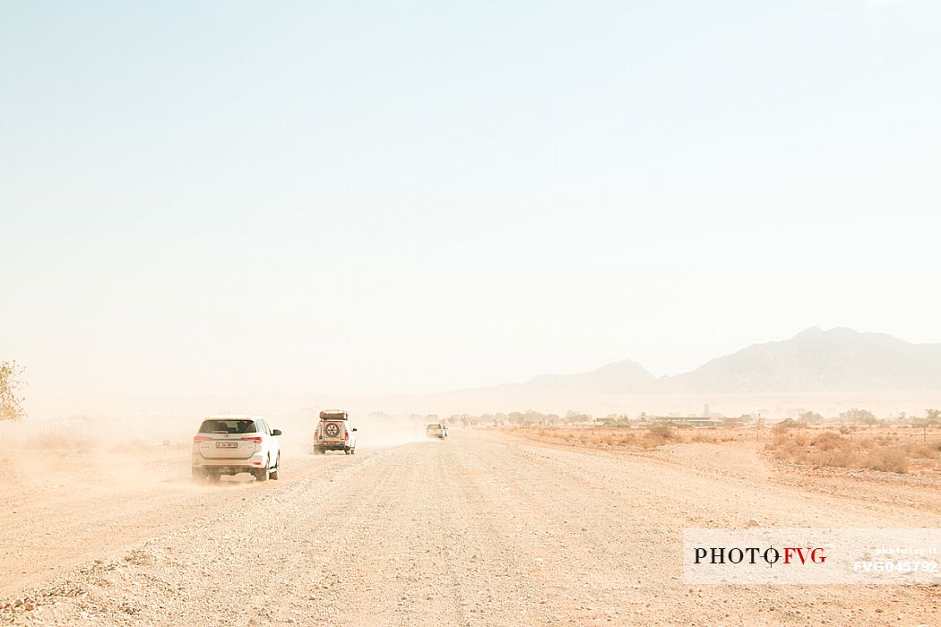 Four 4x4 cars driving in the dust on a gravel road, on the way to Sesriem, Namib Naukluft National Park, Namibia. Africa
