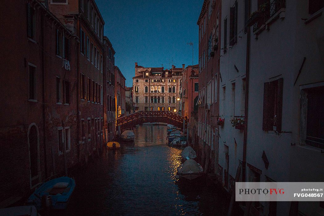 Dusk view on a typical venetian canal with some boats in the foreground and an ancient building lighted with the last light of the day in the background, Venice, Veneto, Italy, Europe