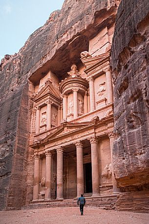 A man walks towards the Treasury or El Khasneh facade in a cloudy day in Petra, Jordan