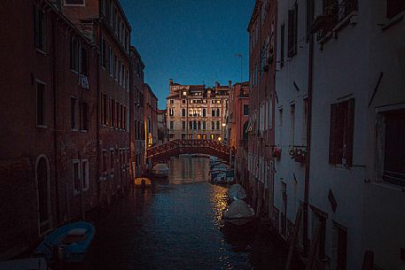 Dusk view on a typical venetian canal with some boats in the foreground and an ancient building lighted with the last light of the day in the background, Venice, Veneto, Italy, Europe