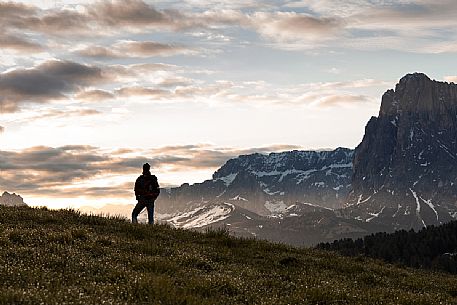 A trekker standing on the slope of a mountain at sunrise with Sella and Sassolungo mountains in the background, Seiseralm, dolomites, Trentino Alto Adige, Italy, Europe