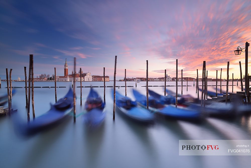 A colorful sunset in the magic mood of Venice with the traditional gondolas in the flow of time, San Giorgio Maggiore church in the background, Venice, Italy