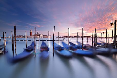 A colorful sunset in the magic mood of Venice with the traditional gondolas in the flow of time, San Giorgio Maggiore church in the background, Venice, Italy