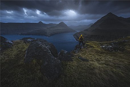 Hiker looking the stormy sunset in the Fjord near Funningur, Eysturoy Island, Faeroe Islands, Denmark 