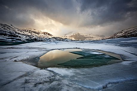 A ray of sunshine during a lightning storm lights up the little Mont Cenis and reflected on a puddle of water on the frozen lake in dissolution