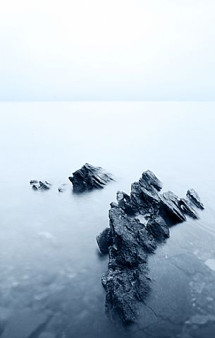 Group of rocks on the shore of the dam of the Mont Cenis lake in the fog