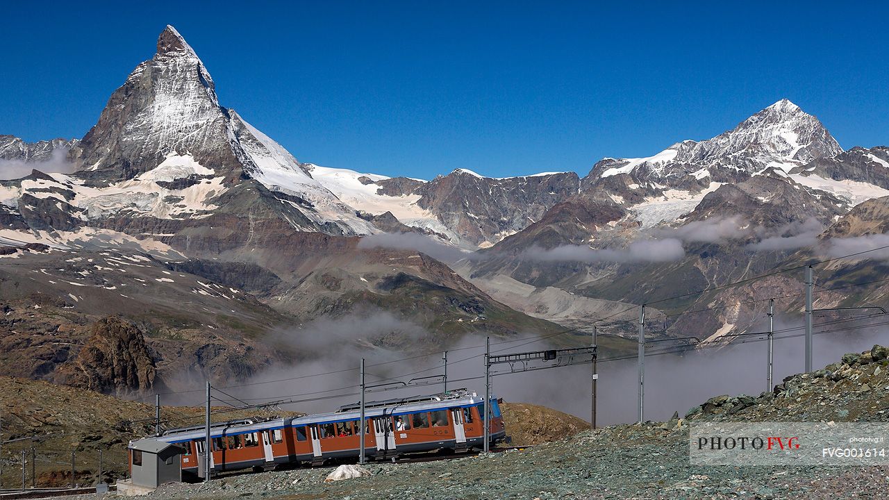 Train of Gornergrat railway arriving at the summit station, in the background  the magnificent Cervino or Matterhorn mountain peak, Zermatt, Valais, Switzerland, Europe