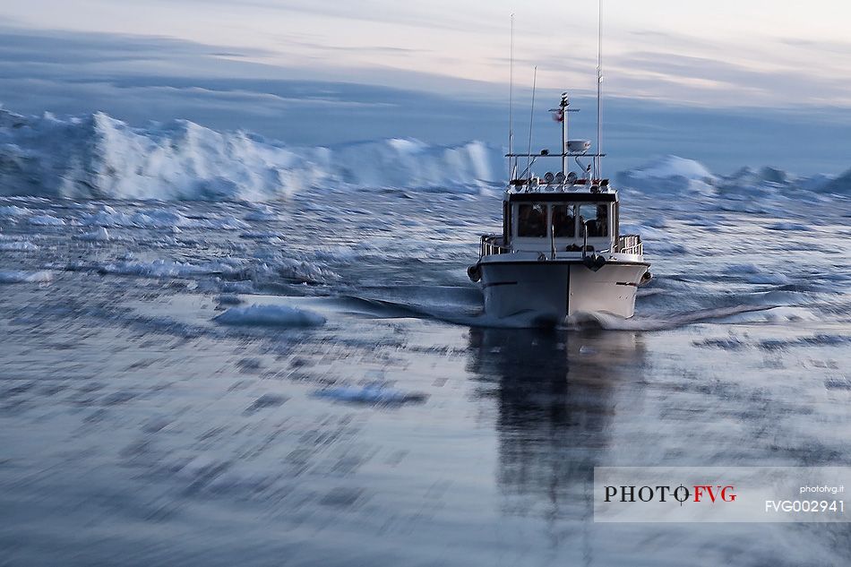 Fish boat moves fast between the ice-water of the sea in front of Illulissat town