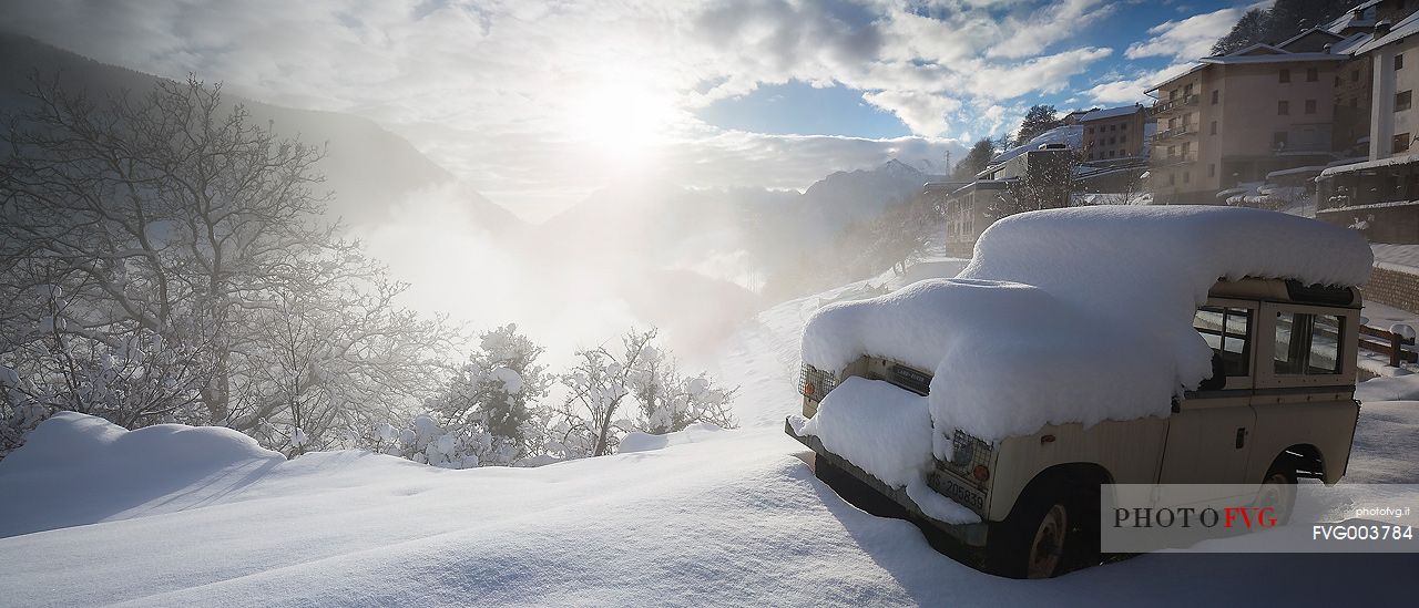An old Land Rover covered by snow in Casso alpine town after an intense snowfall