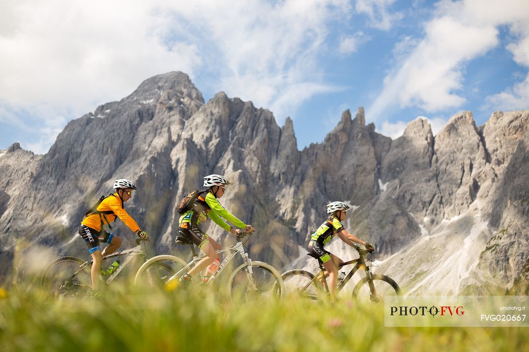 A young mountain bikers come down from Biscia summit, in the background the Sesto Dolomites, Cadore, Italy