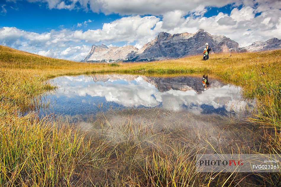 Hikers at lake in Pralongi meadows, in background the Sasso della Croce mountain, Val Badia, Dolomites, South Tyrol, Italy 