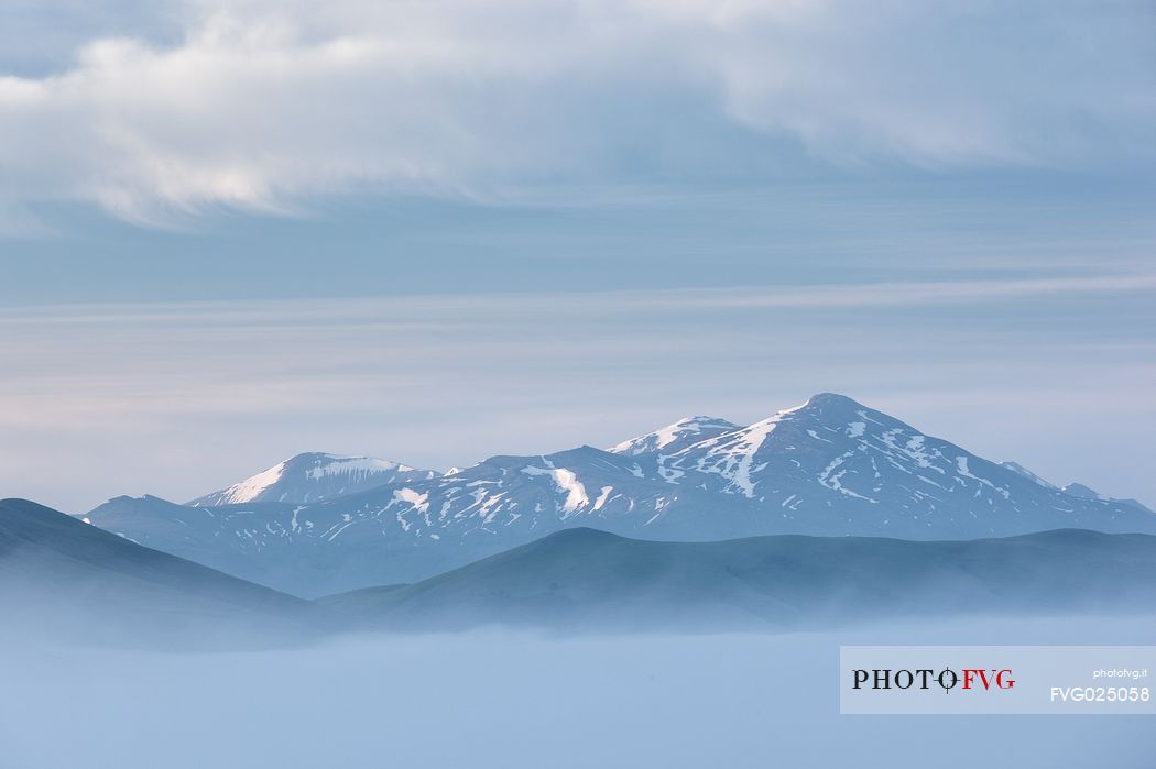 First lights of dawn on Pian Grande Plateau surrounded by great clouds and fog, Castelluccio di Norcia, Sibillini National Park, Italy