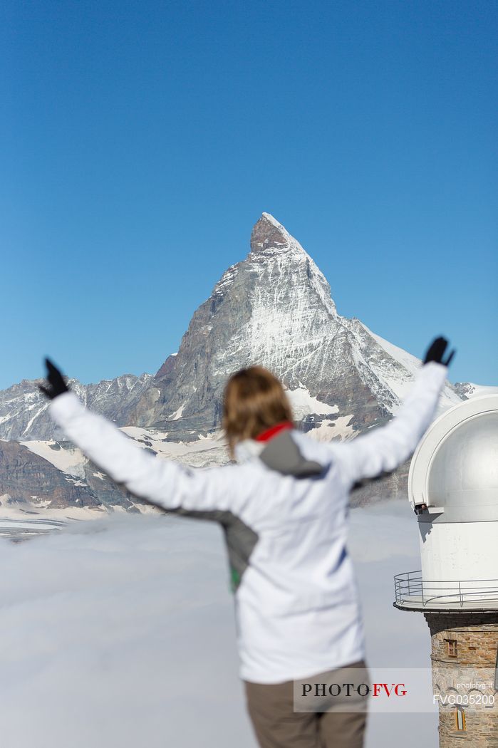 Woman in the top of Gornergrat admiring the Matterhorn or Cervino mountain peak and the astronomic observatory of Klum Hotel, Zermatt, Valis, Switzerland, Europe