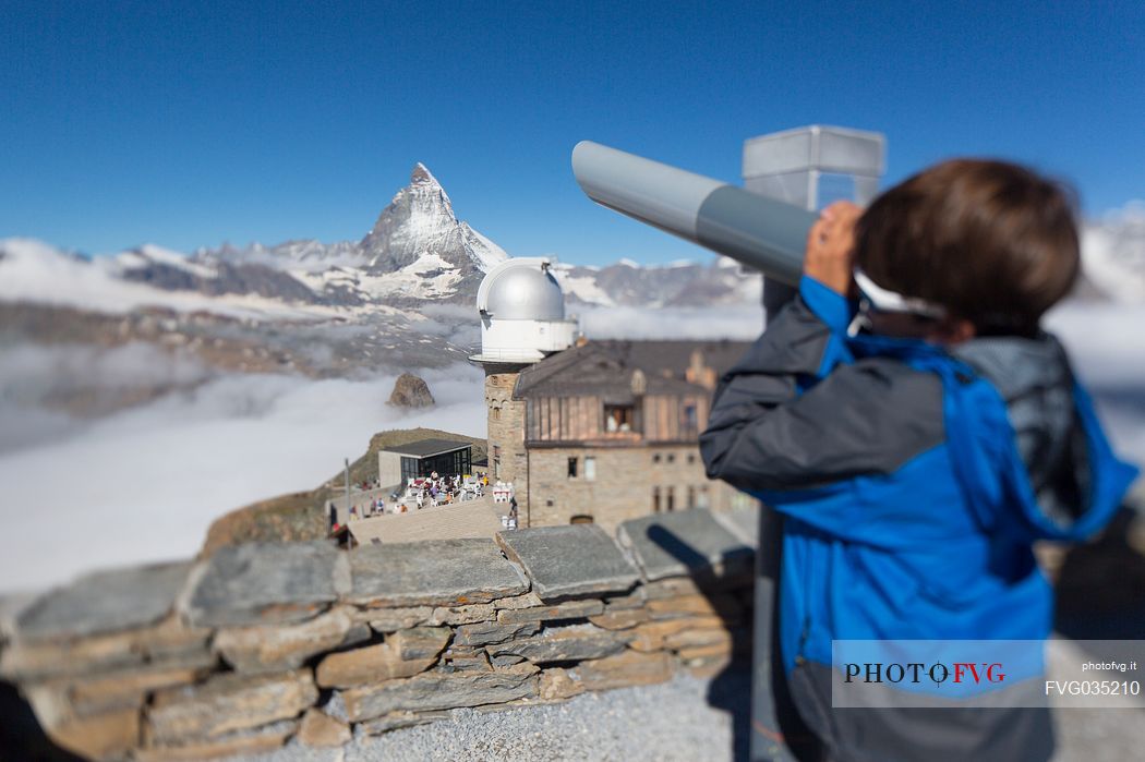 Child in the top of Gornergrat admiring the Matterhorn or Cervino mountain peak with a coin operated binoculars, Zermatt, Valis, Switzerland, Europe