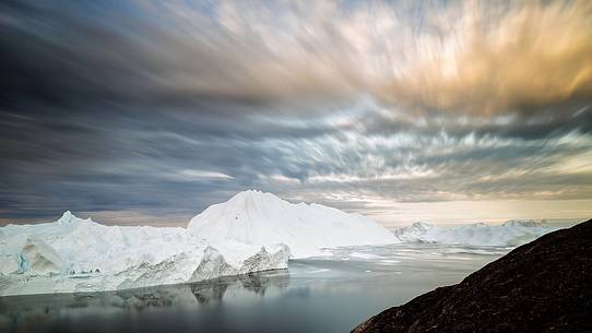 Morning light and coloured clouds on icebergs of Kangerlua Fjord at dawn