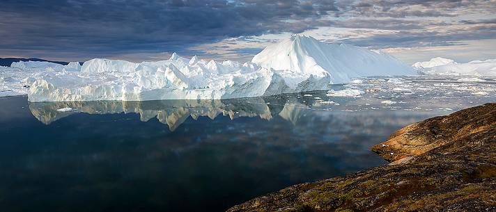 Morning light on icebergs and their reflection on water of Kangerlua Fjord at dawn