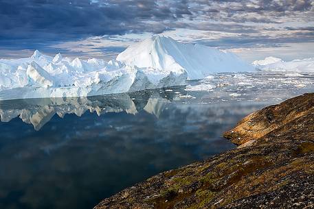 Morning light on icebergs and their reflection on water of Kangerlua Fjord at dawn