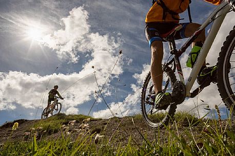 Two young mountain bikers come down from Biscia summit, in the background the Sesto Dolomites, Cadore, Italy