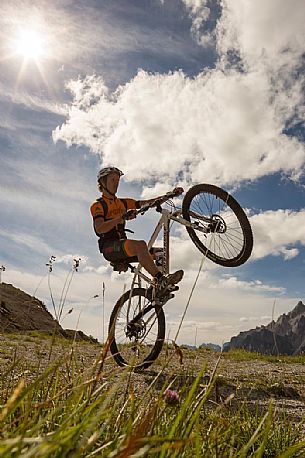 Two mountain bikers come down from Biscia summit, in the background the Sesto Dolomites, Cadore, Italy