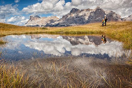 Hikers at lake in Pralongi meadows, in background the Sasso della Croce mountain, Val Badia, Dolomites, South Tyrol, Italy 