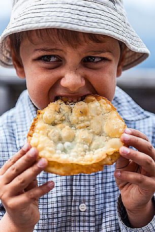 Hungry child eats Turtres, traditional ladin food, South Tyrol, Dolomites, Italy