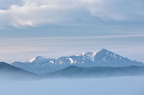 First lights of dawn on Pian Grande Plateau surrounded by great clouds and fog, Castelluccio di Norcia, Sibillini National Park, Italy