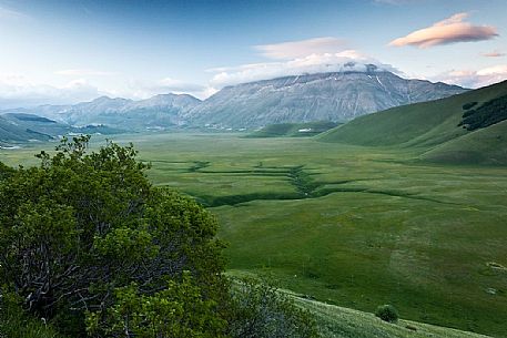 Last lights on Piano Grande Plateau with visible the karst Fosso dei Mergani and in the background Vettore Mount and its fault and the little village of Castelluccio di Norcia, Sibillini National Park, Italy