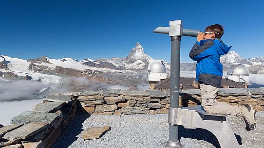 Child in the top of Gornergrat admiring the Matterhorn or Cervino mountain peak with a coin operated binoculars, Zermatt, Valis, Switzerland, Europe
