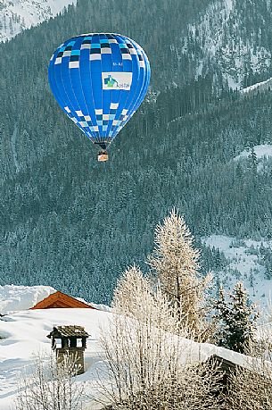 A hot-air balloon flies over the village of Dobbiaco during the balloon festival in Pusteria valley, Dolomites, Trentino Alto Adige, Italy, Europe