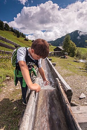 Child plays with natural water that flow in the traditional wooden canal near a water mill, Longiarù, Badia valley, dolomites, Trentino Alto Adige, Italy, Europe