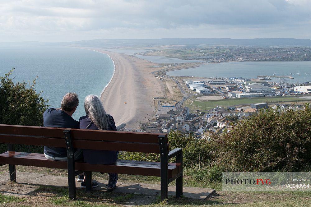 Couple adminirg the panorama from Portland Heights, beautiful viewpoint located on the way to the famous Portland Bill. From Portland Heights you can admire the 17 miles long Chesil beach, also known as Chesil Bank, Dorset, England, UK