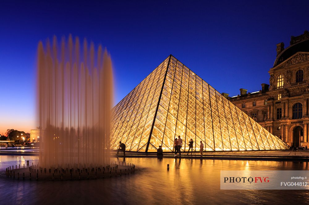 Silhouettes of tourist at sunset lights at the Louvre square with the glass pyramid and the fountain, Paris, France, Europe