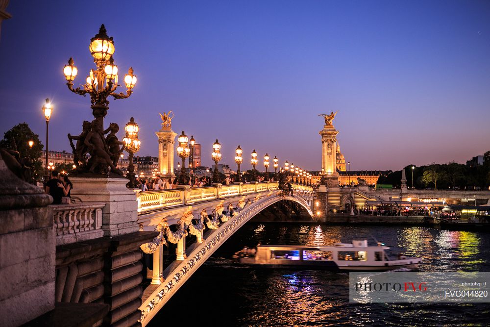 The Alexander III bridge at twilight while passing a Bateau Mouche, Paris, France, Europe