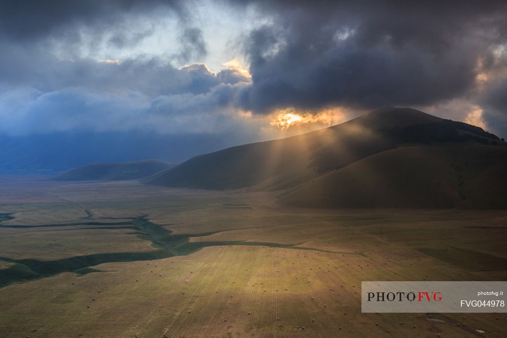 The first rays of sun illuminate the Pian Grande plain of Castelluccio di Norcia at dawn, Umbria, Italy, Europe