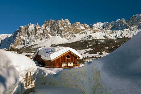 A view of Cortina D'Ampezzo from Pocol with a cottage covered by snow in the foreground and mount Cristallo and Pomagagnon in the background