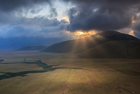 The first rays of sun illuminate the Pian Grande plain of Castelluccio di Norcia at dawn, Umbria, Italy, Europe