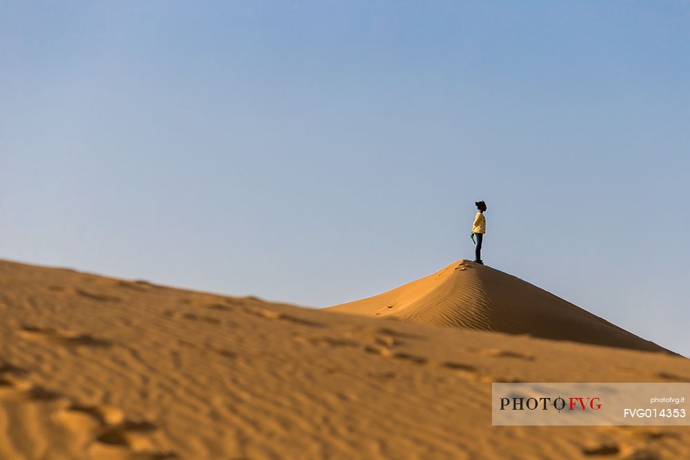A young girl looking at the horizon from above a sand dune