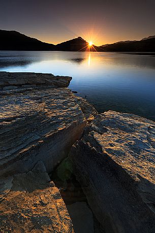 At dawn the sun peeks out behind the lake of Campotosto that seems to be preparing for a day full of light, Gran Sasso and monti della Laga national park, Abruzzo, Italy