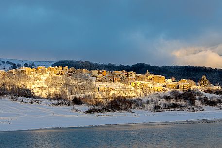 The village of Mascioni illuminated during the sunset and the Capotosto lake, Gran Sasso and Monti della Laga national park, Abruzzo, Italy