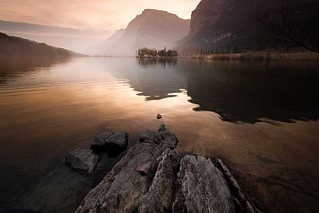 Misty sunset reflection on Toblino lake in autumn, in the background the Toblino castle, Trentino, Italy, Europe