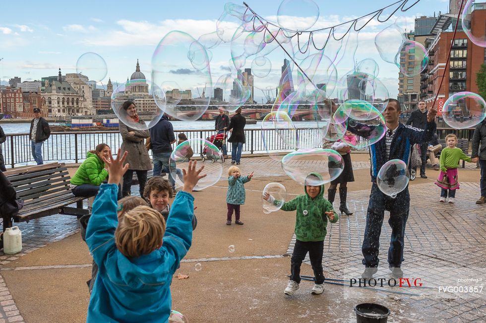 Some children play with big soap bubbles in a little square on the south river of Thames